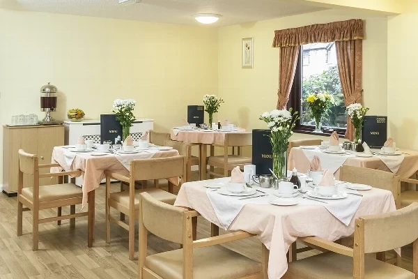 A dining room with tables laid with white cloths and fresh flowers