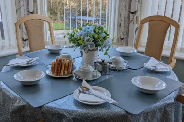 A dining table laid for afternoon tea with cakes and fresh flowers