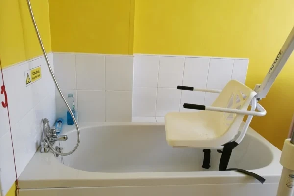 An assisted bathroom with a bath hoist seat and grab rails
